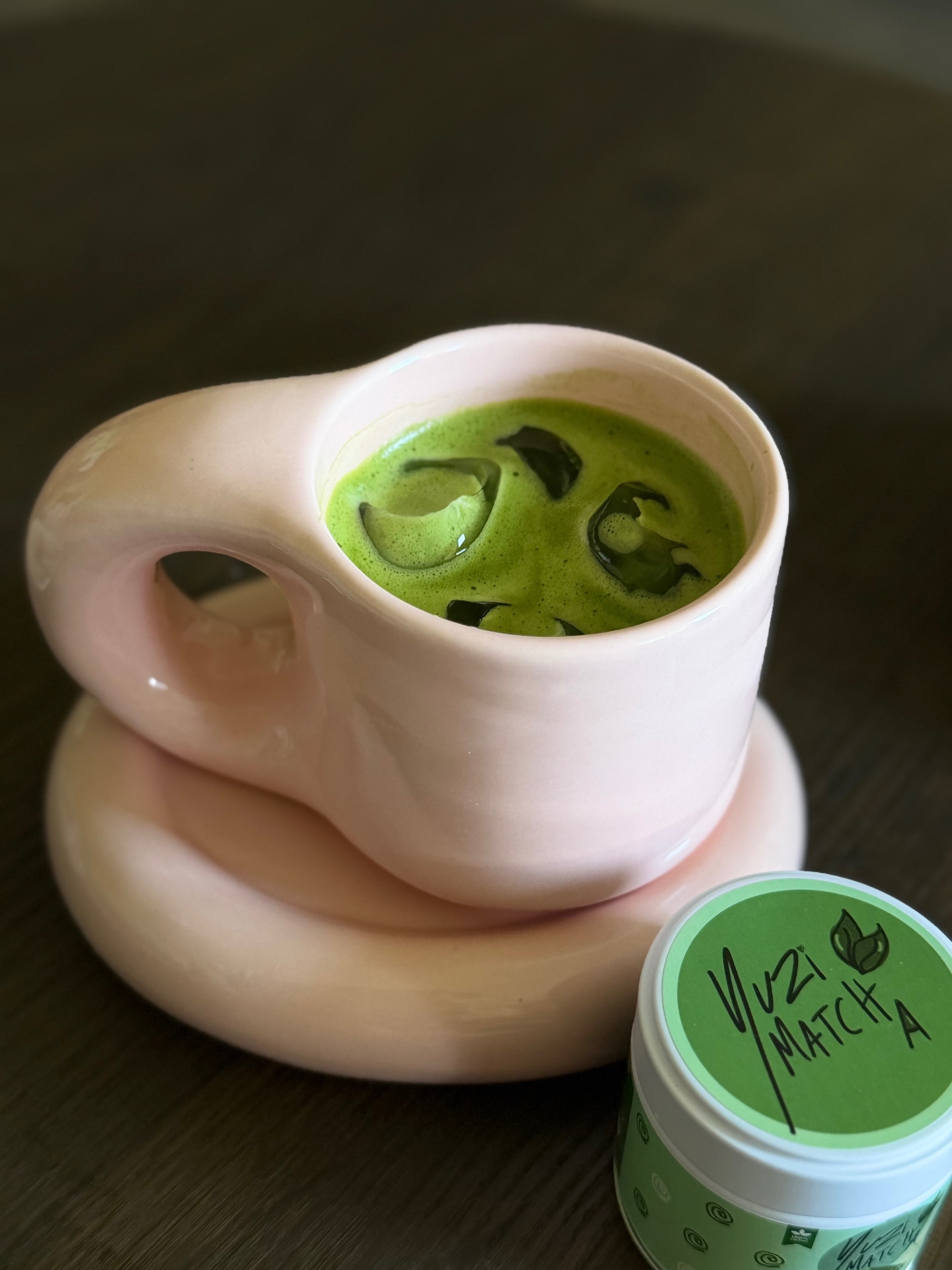 Iskall matcha latte i rosa kopp bredvid en Yuzi Matcha burk